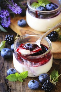 Panna cotta with blueberry and blackberry coulis - Traditional homemade Italian dessert served in glass jars and decorated with fresh berries and a sprig of mint on dark rustic wooden background